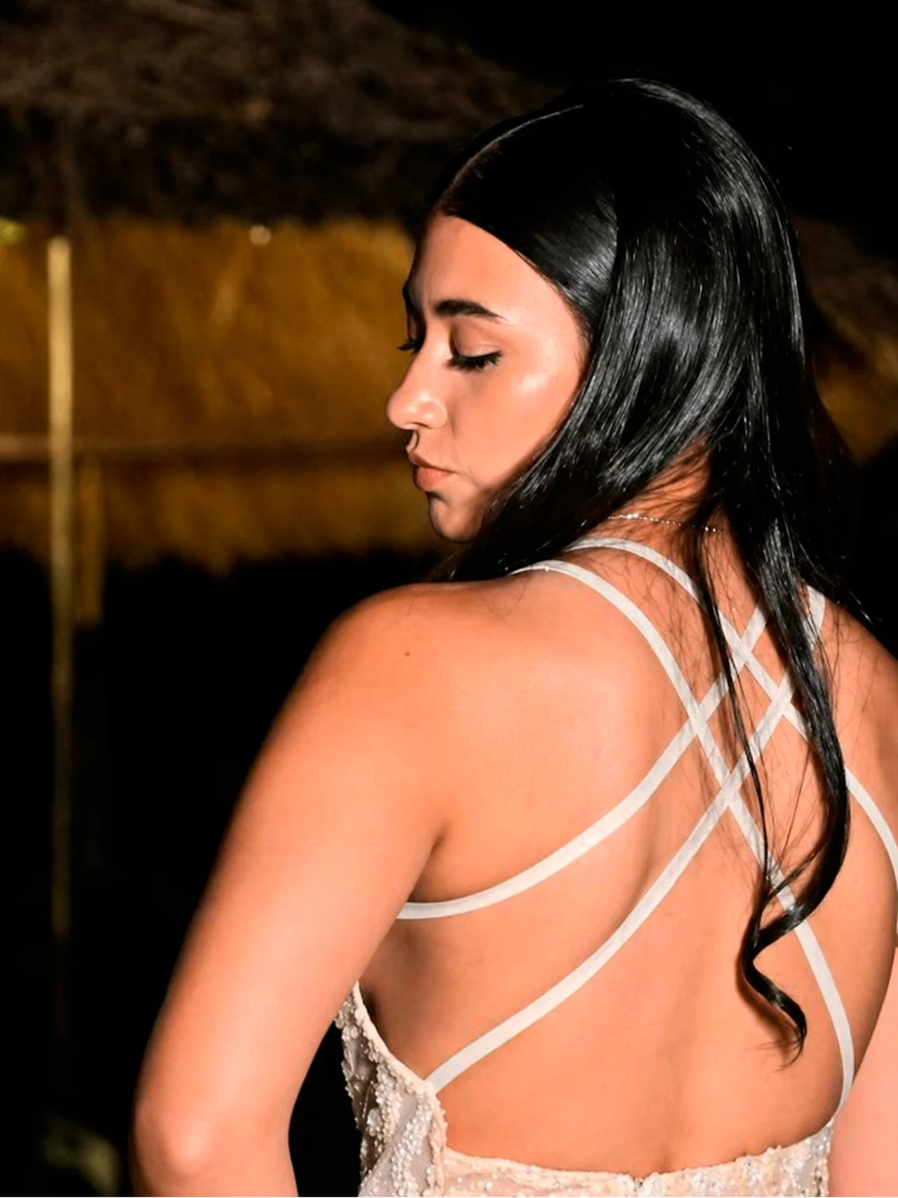 Vista posterior de un peinado social elegante en cabello largo y oscuro con un acabado liso, pulido y una onda definida hacia las puntas. El look destaca la salud y el brillo capilar para el sitio de Meli Figarola, complementado con un vestido de gala con espalda descubierta y tirantes cruzados en un entorno nocturno.